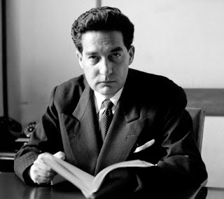 Octavio Paz: Retrato em preto e branco de um homem de terno segurando um livro aberto em uma mesa.