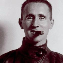 Bertolt Brecht: Retrato em close-up de um homem com cabelos curtos, vestindo uma jaqueta de gola alta e fumando um charuto.