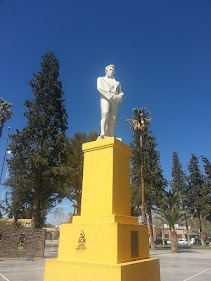 Bernardo O'Higgins: Estátua branca sobre um pedestal amarelo alto em uma praça com árvores e céu azul ao fundo.