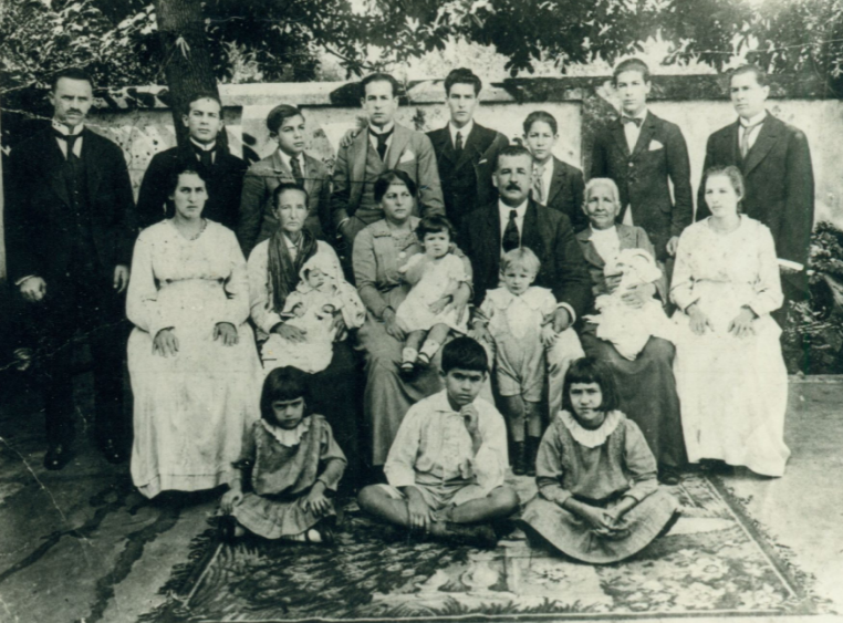 desconhecido: Uma fotografia antiga em preto e branco de uma família numerosa reunida para um retrato ao ar livre.