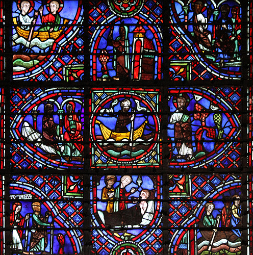 Fotografia em close-p de um vitral medieval colorido, retratando várias cenas religiosas e bíblicas em painéis individuais, com tons predominantes de azul e vermelho.