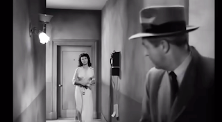 Sterling Hayden, Marie Windsor: Uma cena de filme em preto e branco mostrando um homem de chapéu em primeiro plano observando uma mulher saindo de uma porta ao fundo de um corredor.
