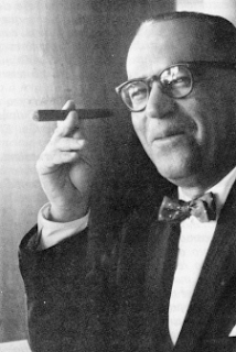 Guimarães Rosa: Retrato em preto e branco de um homem usando óculos e gravata borboleta, segurando um charuto.