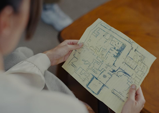 Uma pessoa segurando um papel com o desenho feito à mão de uma planta baixa ou mapa de um edifício.