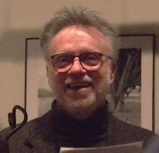 unknown: Retrato de um homem sorridente de óculos e barba curta.