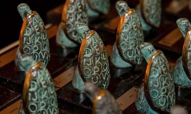 Várias estatuetas de bronze em formato de casco de tartaruga com letras do alfabeto gravadas, representando o Prêmio Jabuti.