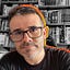 António Araújo: Retrato de um homem com óculos em frente a uma estante de livros.