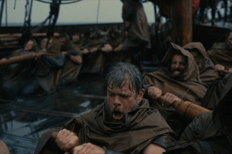 Matt Damon: Uma cena de filme mostrando homens exaustos remando em um grande barco sob chuva.