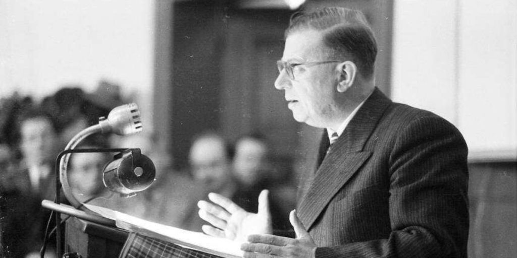 Jean-Paul Sartre: Fotografia em preto e branco de Jean-Paul Sartre discursando atrás de um púlpito com microfones.