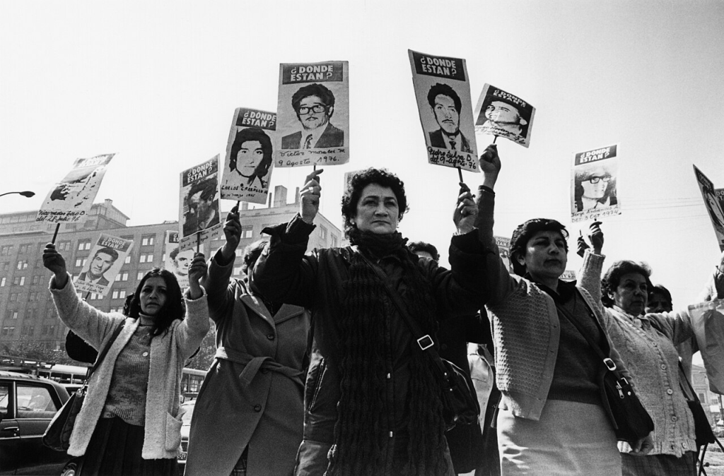 Fotografia em preto e branco de mulheres em um protesto segurando cartazes com fotos de pessoas desaparecidas e a frase '¿Donde Estan?', referindo-se aos desaparecidos políticos no Chile.