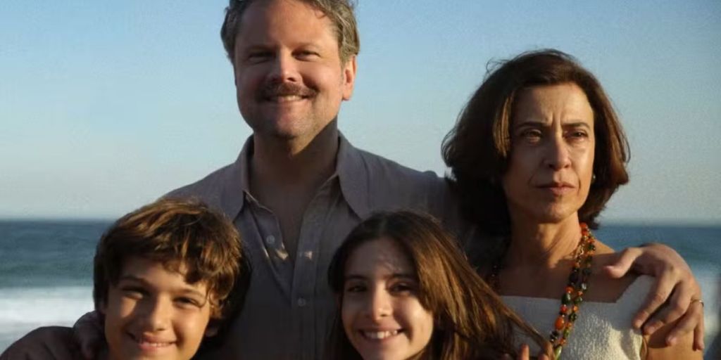 Selton Mello, Fernanda Torres: Uma fotografia de cena do filme 'Ainda Estou Aqui' mostrando os atores Selton Mello e Fernanda Torres com crianças em uma praia.