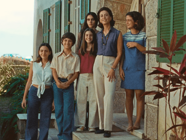 Fernanda Torres: Uma mulher e cinco crianças/jovens posam para uma foto em frente a uma casa com janelas de veneziana verde. Cena do filme 'Ainda Estou Aqui'.