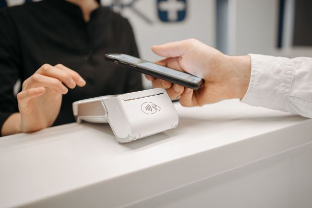 unknown: Uma pessoa realizando um pagamento por aproximação utilizando um smartphone em um terminal de cartão sobre um balcão branco.