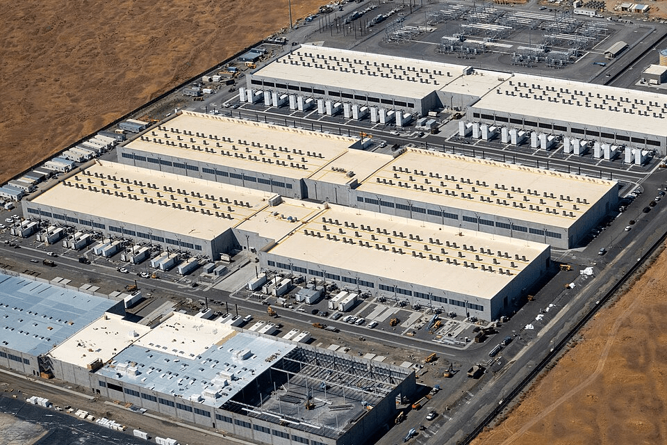 Vista aérea de um grande complexo industrial ou data center com vários edifícios longos e equipamentos de ventilação no telhado.