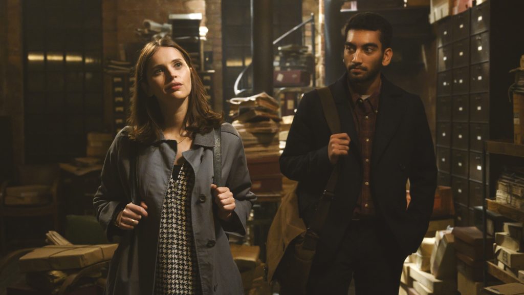 Felicity Jones, Nabhaan Rizwan: Cena do filme 'A Última Carta de Amor' mostrando um homem e uma mulher em um arquivo ou biblioteca antiga.