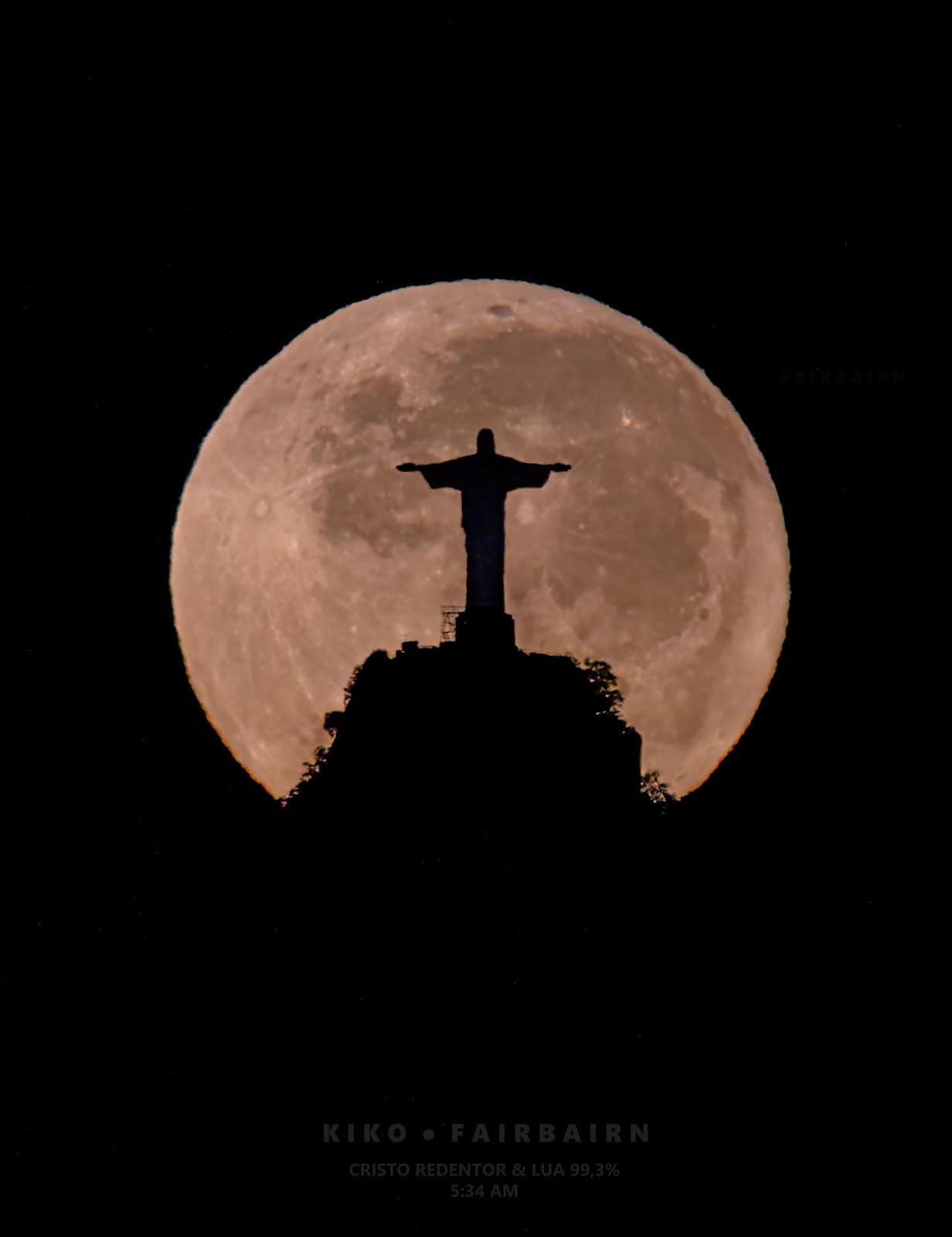 A silhouette of the Christ the Redeemer statue stands atop a mountain peak against the backdrop of a large, full moon.