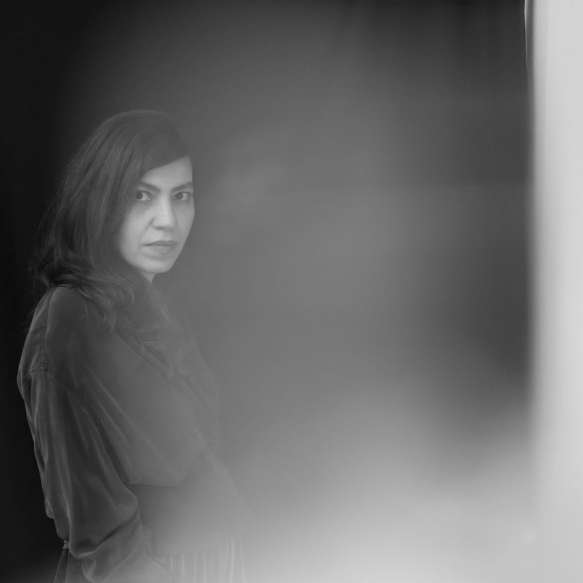 Inês Pedrosa: Retrato em preto e branco de uma mulher com cabelos escuros, olhando para a câmera com um efeito de desfoque/névoa em parte da imagem.