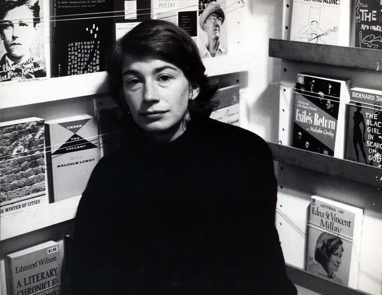 Mary Oliver: Retrato em preto e branco de uma mulher em uma livraria, com várias capas de livros visíveis nas prateleiras ao fundo.