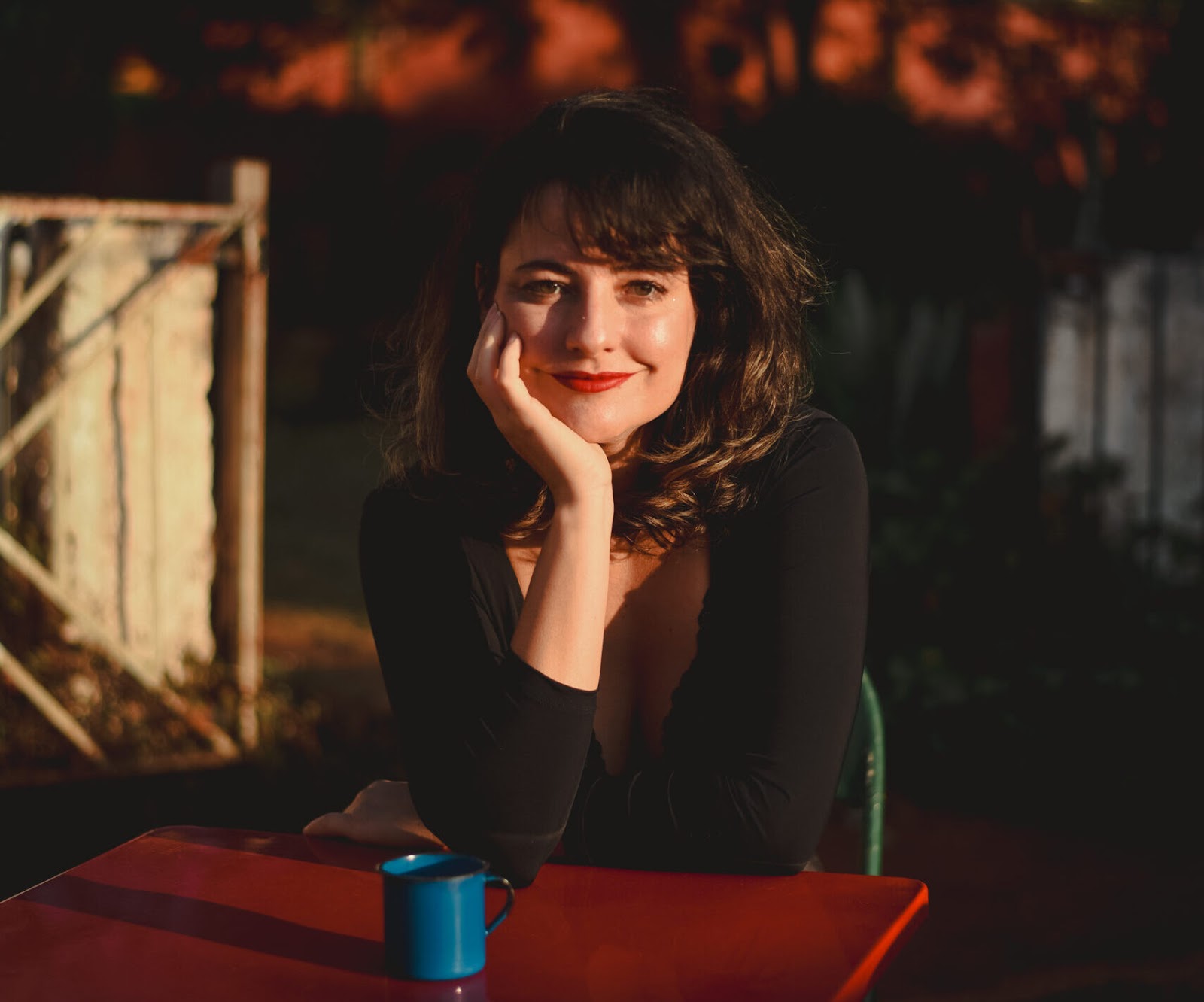 unknown: Retrato de uma mulher sentada à mesa com uma caneca azul, sob a luz do pôr do sol.