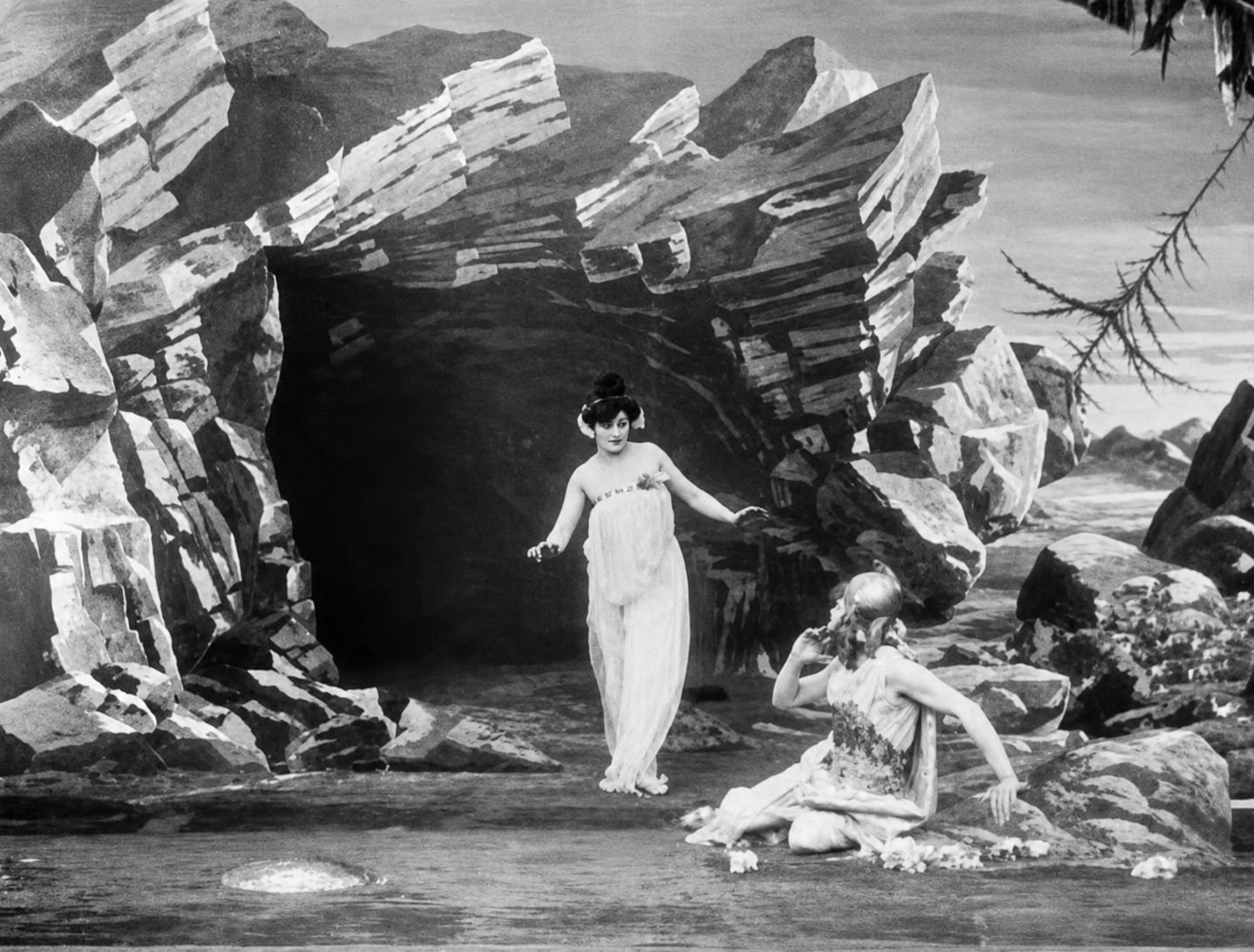 Kiki de Montparnasse: Cena em preto e branco do filme mudo L'Étoile de mer (1928), mostrando duas mulheres em um cenário artístico de caverna e rochas.