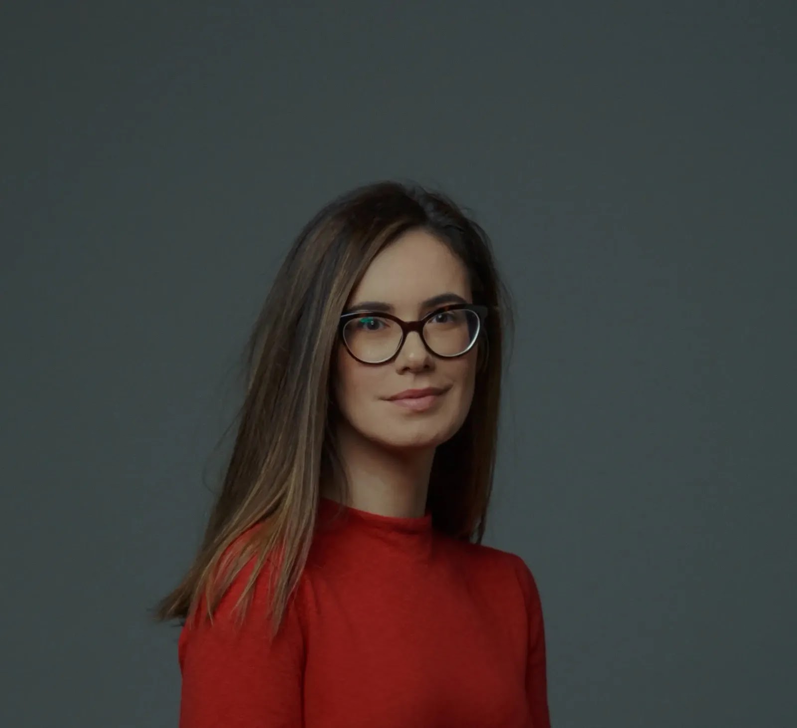 unknown: Retrato de uma mulher com óculos e blusa vermelha contra um fundo cinza.