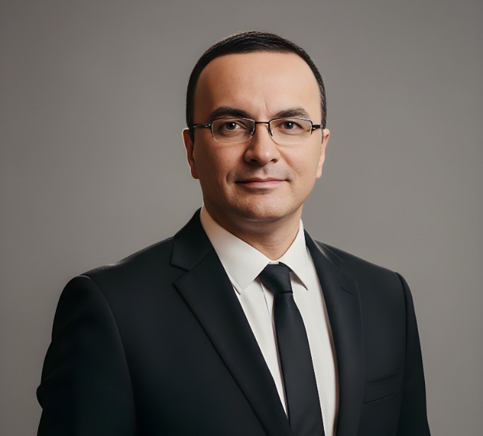 desconhecido: Retrato de estúdio de um homem de óculos, usando terno preto, camisa branca e gravata preta, contra um fundo cinza.